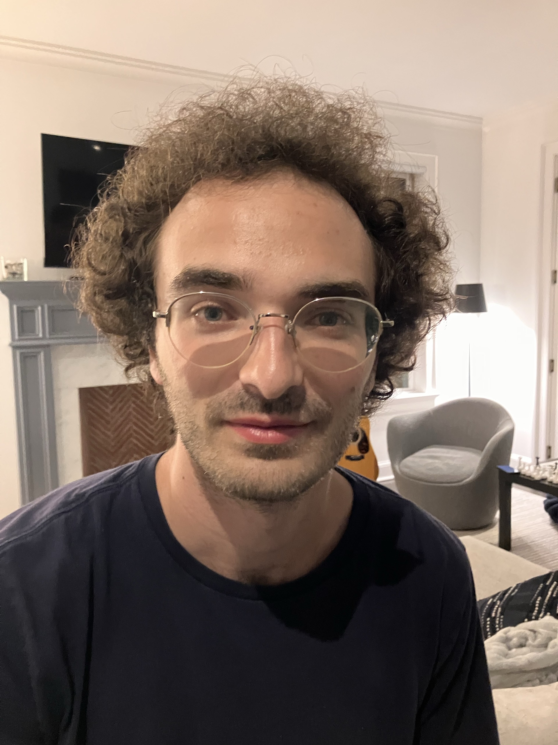 Portrait of a person with curly hair and glasses in a living room